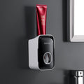 Automatic Toothpaste Squeezer in black and white plastic, wall-mounted with a front dispensing button and red toothpaste tube