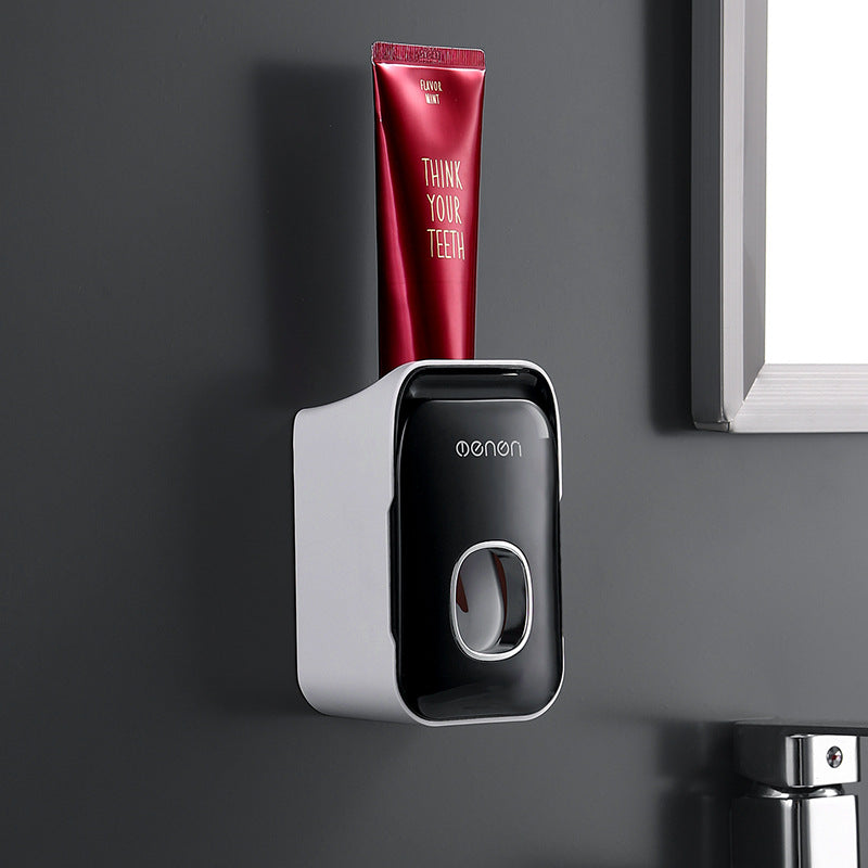 Automatic Toothpaste Squeezer in black and white plastic, wall-mounted with a front dispensing button and red toothpaste tube
