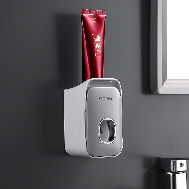 Automatic Toothpaste Squeezer in light gray plastic with a rounded wall-mounted dispenser holding a red toothpaste tube