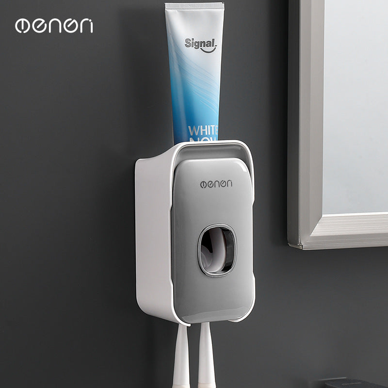 Automatic Toothpaste Squeezer in gray plastic with a white trim, holding a toothpaste tube and two toothbrushes