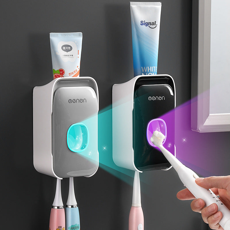 Automatic Toothpaste Squeezer in gray and black plastic, with wall-mounted dispensers, central push openings, and toothbrush holders.