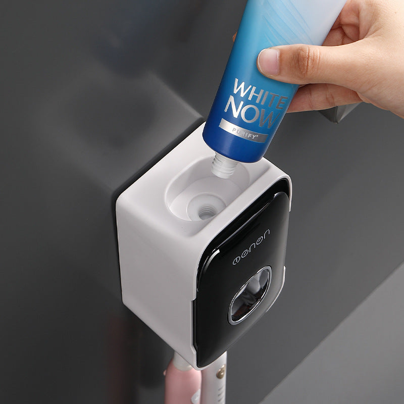 Automatic Toothpaste Squeezer in white plastic with a glossy black front, dispensing toothpaste from a blue tube