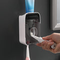 Automatic Toothpaste Squeezer in white plastic with a dark transparent front, dispensing toothpaste onto a toothbrush