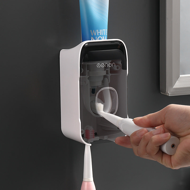 Automatic Toothpaste Squeezer in white plastic with a dark transparent front, dispensing toothpaste onto a toothbrush