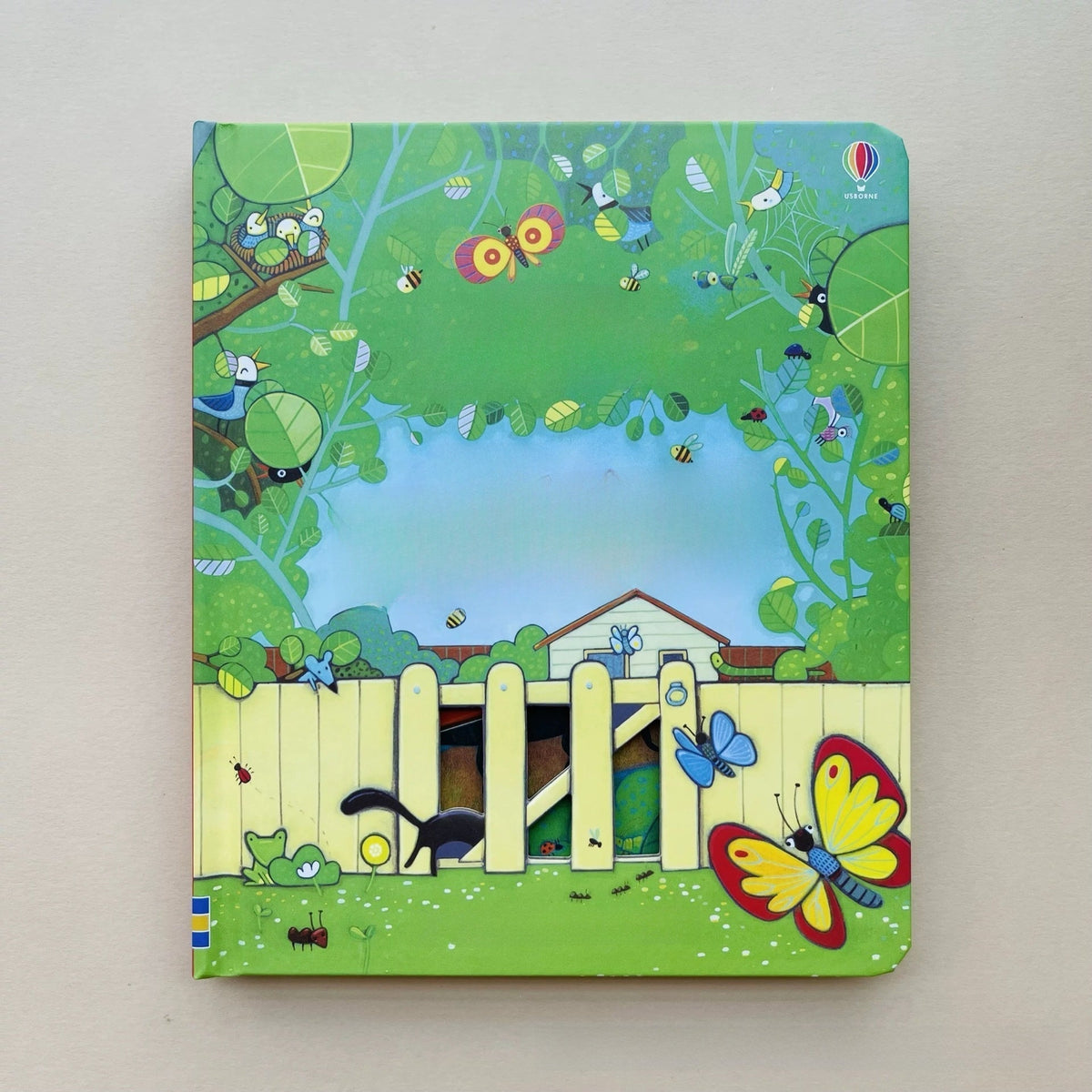 Children’s peek-through board book in green with a colorful garden scene, butterflies, bees, and cutout fence details; Educational  Picture Books