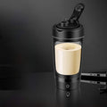 Electric Protein Shaker Cup in black with a clear Tritan body, cream-colored drink inside, and flip-top lid