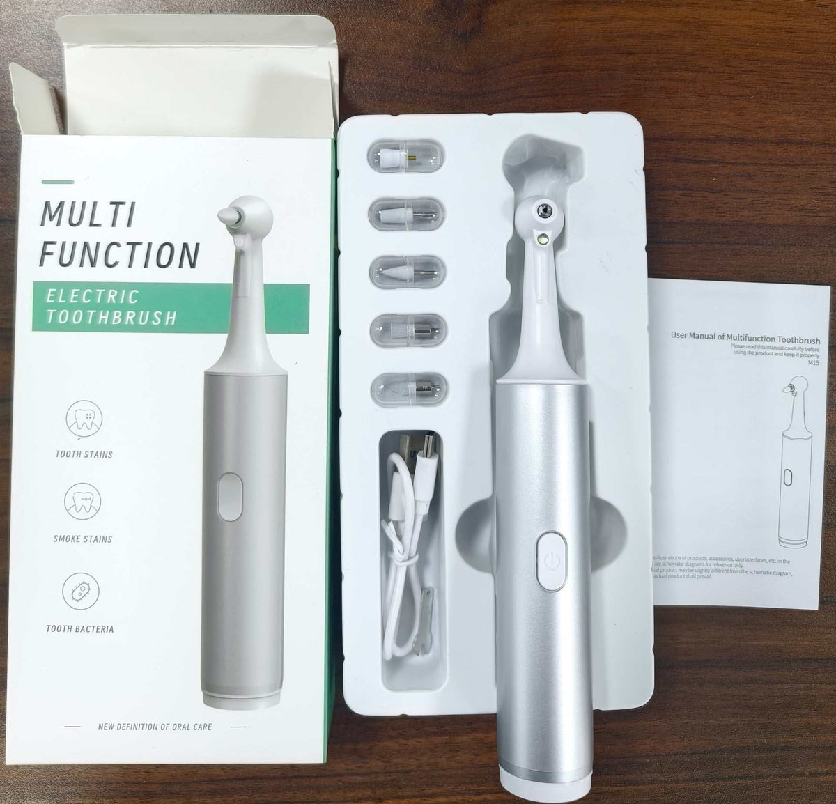 Electric Tooth Cleaner in silver with a smooth cylindrical handle, rounded cleaning head, removable tips and charging cable