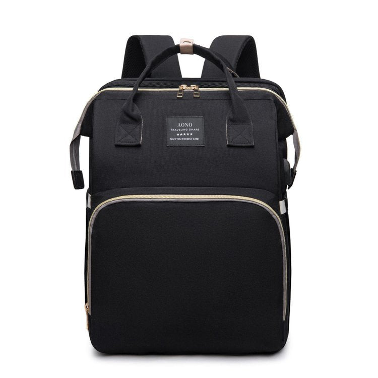 Foldable Baby Bed shown as a black Oxford cloth backpack with beige piping, top handles, shoulder straps and zip pockets