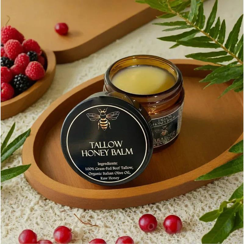 Honey Tallow Moisturizing Balm in an amber glass jar with a black-and-gold label, alongside fresh oranges and leaves.