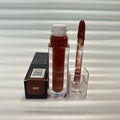 Huda Beauty Moisturizing lip gloss in a clear rectangular tube, shown in a deep brown shade with matching applicator and box