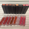 Huda Beauty Moisturizing lip glosses in clear rectangular tubes, with black boxes and a range of red, pink, nude and brown shades