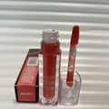 Huda Beauty Moisturizing lip gloss in a clear rectangular tube with deep red color and matching applicator wand