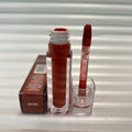 Huda Beauty Moisturizing lip gloss in deep reddish brown, shown with clear tube, doe-foot applicator and She Fire box