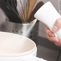 Kitchen Oil Spray Bottle with a white plastic press sprayer releasing a fine mist over a bowl
