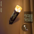 Minecraft Ore lamps torch with a glowing yellow-orange pixelated head and dark block-patterned handle, mounted on a wall