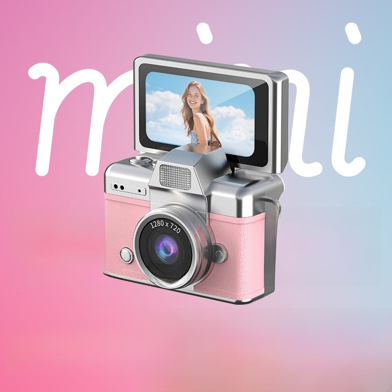 Miniature Digital Camera with a pink textured body, silver accents, a round lens and a flip-up screen