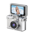 Miniature Digital Camera in silver and white textured plastic, with a large lens, black trim and a flip-up screen
