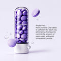 Purple Toothpaste Tablets in smooth lavender-purple pressed form, displayed in a clear cylindrical dispenser with a white base.