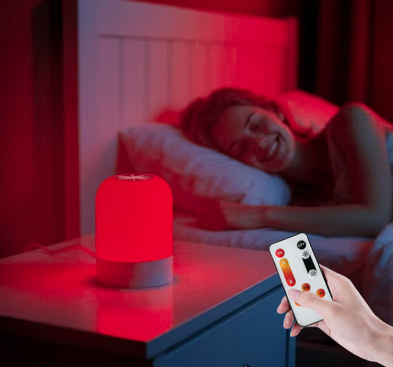 Red Light Therapy Lamp with a compact red cylindrical shade and gray base, operated by a handheld remote beside a bed