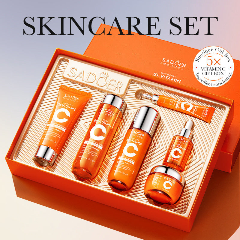 Skincare set featuring orange SADOER Vitamin C Skincare tubes, bottles, and jar with silver caps in a striped gift box.