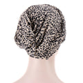 Printed headscarf cap in beige polyester with dense black leopard spots and gathered fabric; Short braids can be hidden beneath it.