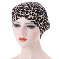 Headscarf cap in white with black and brown leopard print, gathered fabric, and a wrapped turban-style front. Short braids can be hidden