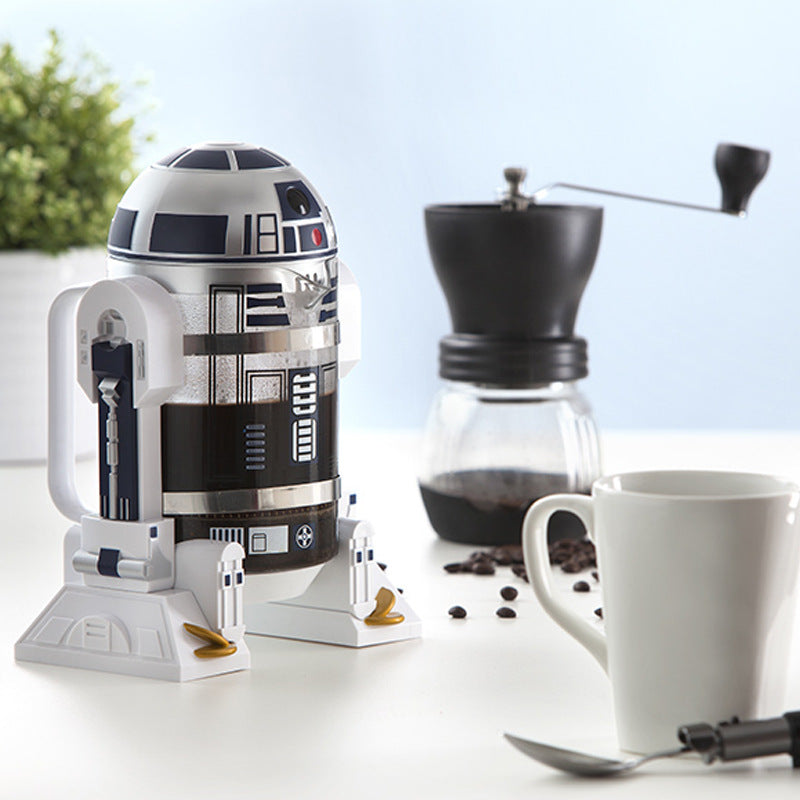 French press coffee maker shaped like a Star Wars R2D2 Robot, with a white plastic shell, silver and black panels, and glass carafe.