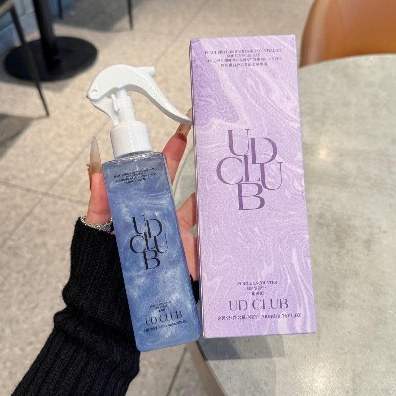 UD CLUB Pearl Protein smoothing hair spray in a translucent blue bottle with white trigger and matching pink-purple marbled box