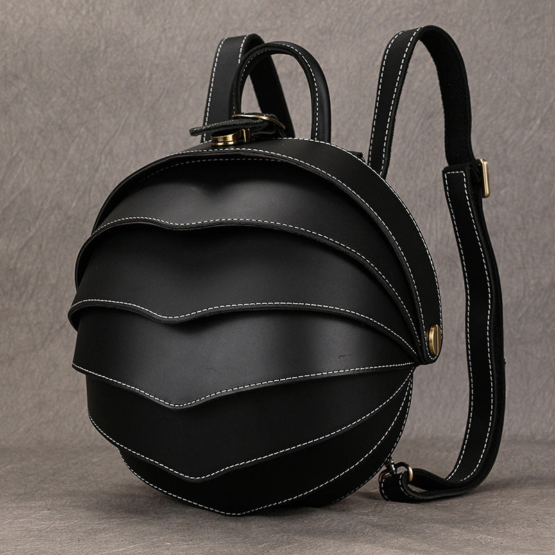 Vintage Genuine Leather backpack in black with a rounded beetle-inspired shape, layered curved panels, white stitching, and adjustable straps