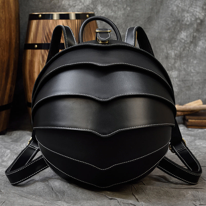 Backpack in black genuine leather with rounded beetle-inspired shell, layered curved panels, and contrasting white stitching