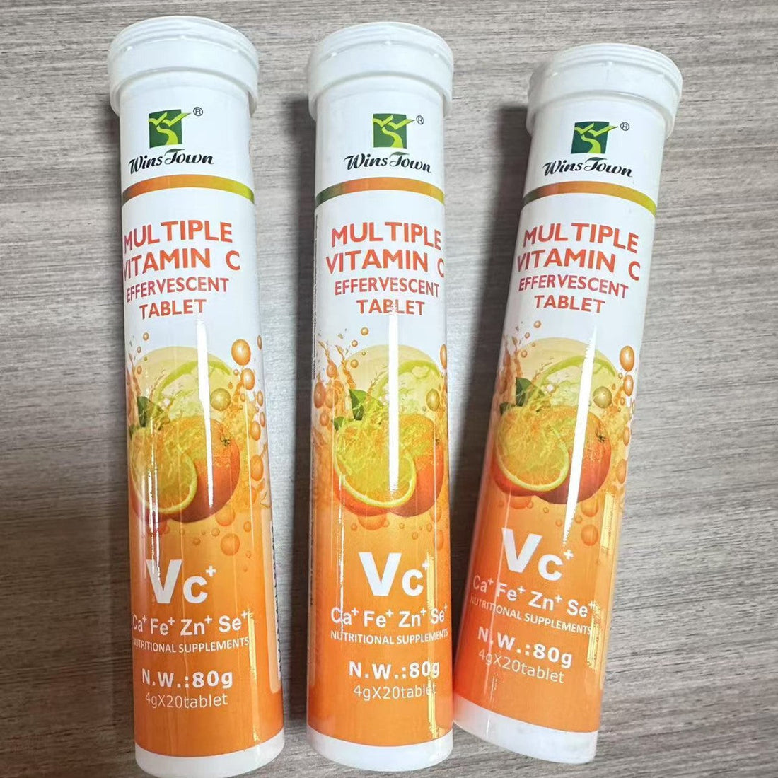 Vitamin C Tablets in three white plastic tubes with orange citrus graphics and effervescent tablet labels.